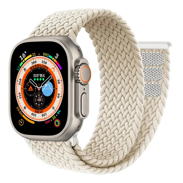 A close-up image of the Apple Watch Adjustable Loop Band. The band features a sleek, continuous loop design made of stretchable woven material that creates a comfortable, snug fit against the wrist. The innovative pull tab mechanism allows for precise size adjustment without buckles or clasps. The band's textured fabric displays fine diagonal weave patterns and appears in the signature Apple minimalist aesthetic. The end of the band connects seamlessly to the Apple Watch housing, emphasizing the clean, unin